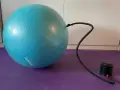 Niebieska piłka fitness podłączona do pompki na fioletowej macie.