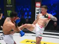 Zacięta walka na KSW 115 karta walk. Zawodnik w białych spodenkach wykonuje wysokie kopnięcie, przeciwnik blokuje je rękawicą.