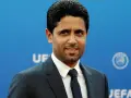 Nasser Al-Khelaifi w garniturze na tle niebieskiej ściany z logo UEFA.