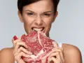 Kobieta z dziką miną wgryza się w surowy kawałek mięsa. Czy można brać białko bez treningu?
