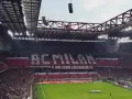 Trybuna stadionu San Siro w Mediolanie wypełniona kibicami AC Milan, tworzącymi napis "AC MILAN" i transparent "FOSSI DEI LEONI, VECCHIESTE IL MIO CUORE LONTANO DA TE".