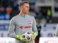 Bramkarz w szarej bluzie z orłem i napisem ORLEN, trzymający piłkę. Kolejny z polscy piłkarze za granicą, gotowy do gry.