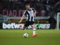 Piłkarz Jesper Karlström w czarno-białej koszulce Udinese Calcio kopie piłkę na zielonej murawie stadionu.