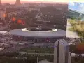 Donbass Arena w blasku zachodzącego słońca, otoczona miejskim krajobrazem i tłumami ludzi.