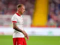 Kamil Grosicki w białej koszulce z orzełkiem i czerwonych spodenkach, gotowy do gry. Jego obecne drużyny to Polska i Pogoń Szczecin.