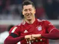 Piłkarz Robert Lewandowski w czerwonej koszulce Bayernu Monachium, uśmiecha się i zaciska pięści.