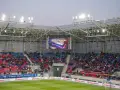 Widownia na stadionie Odra Opole podczas meczu otwarcia. Kolorowe trybuny i wielki ekran z napisem "Mecz otwarcia Itaka Areny".