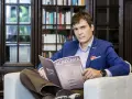 Mężczyzna w garniturze czyta magazyn "Academia Space" w bibliotece. W tle regały z książkami.
