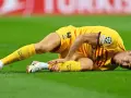 Piłkarz w żółtej koszulce leży na trawie, trzymając się za nogę. Wygląda na to, że Robert Lewandowski kontuzja uniemożliwiła mu dalszą grę.