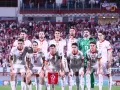 Piłkarze reprezentacji Polski w białych strojach, gotowi do gry. Tłum kibiców na trybunach, biało-czerwone barwy narodowe.