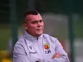Trener Jagiellonii, z rękami skrzyżowanymi na piersi, w szarej kurtce z herbem klubu.