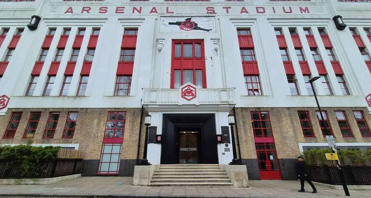 Dawny stadion Arsenalu w Highbury, z charakterystycznym napisem "ARSENAL STADIUM" i czerwonymi akcentami.