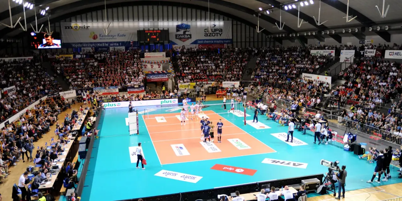 Widownia kibicuje podczas meczu siatkówki ZAKSA. Pełna hala, zawodnicy na boisku, emocje sięgają zenitu.