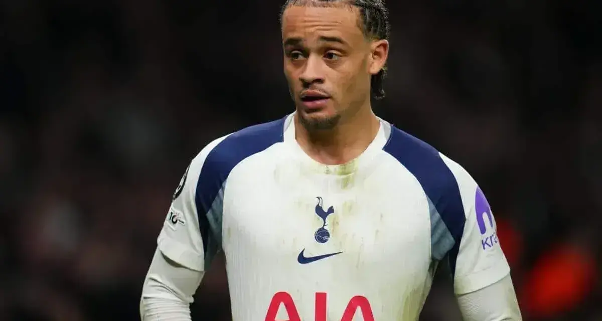 Piłkarz Tottenhamu w białej koszulce z granatowymi wstawkami, gotowy do gry przeciwko Luton Town.