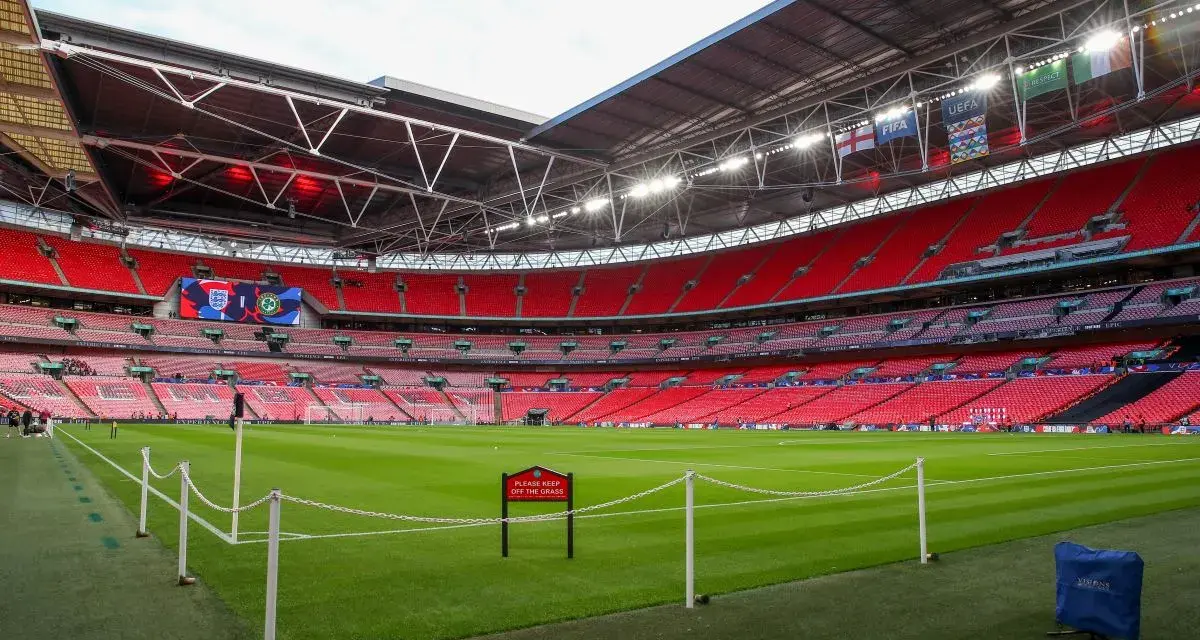 Pusta, czerwona trybuna stadionu Wembley, największego stadionu na świecie, z zieloną murawą i tabliczką "Prosimy nie wchodzić na trawę".