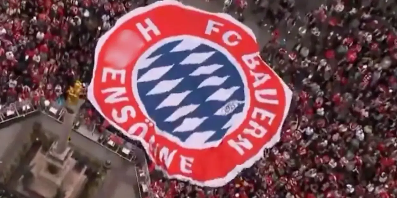 Ogromna flaga z herbem FC Bayern Monachium niesiona przez tłum kibiców.