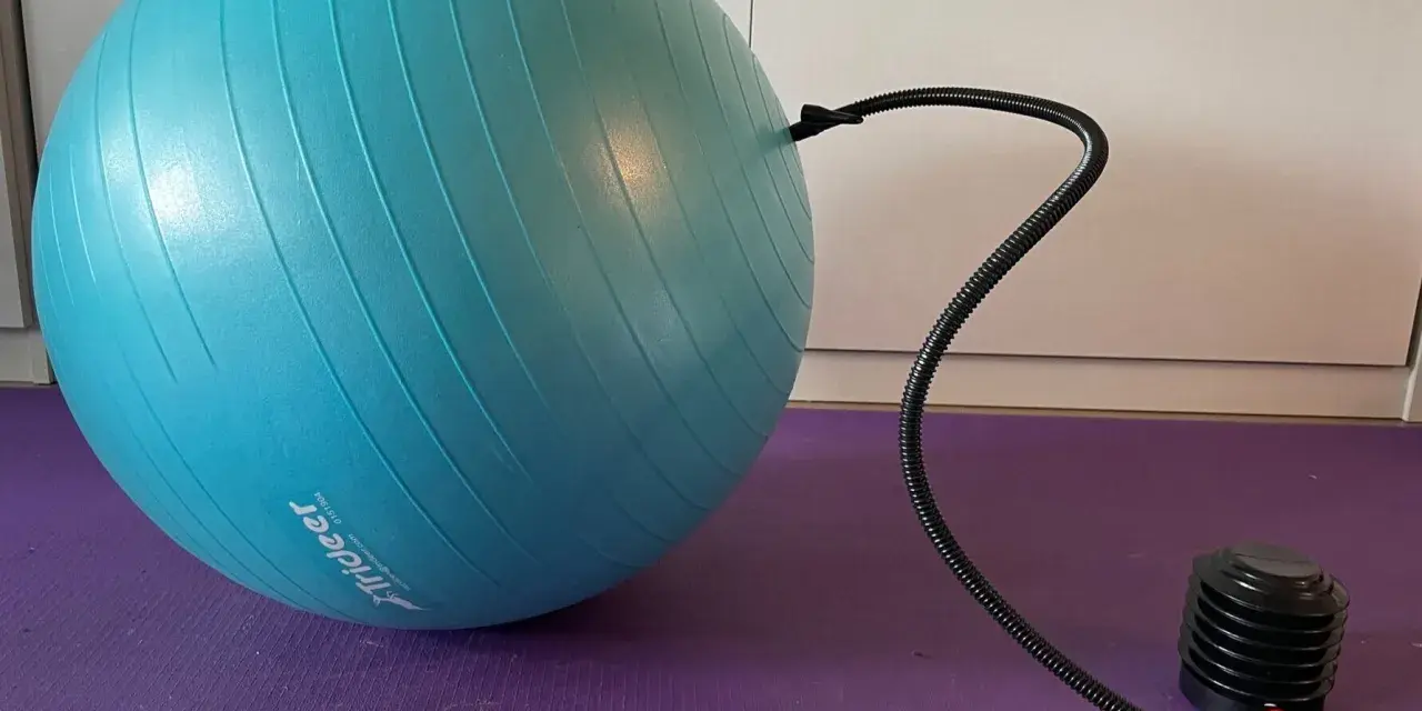 Niebieska piłka fitness podłączona do pompki na fioletowej macie.