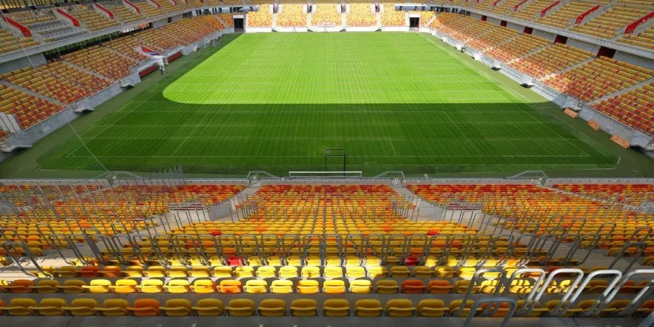 Pusta trybuna stadionu Jagiellonii, z żółtymi i czerwonymi siedzeniami. Pojemność obiektu robi wrażenie.