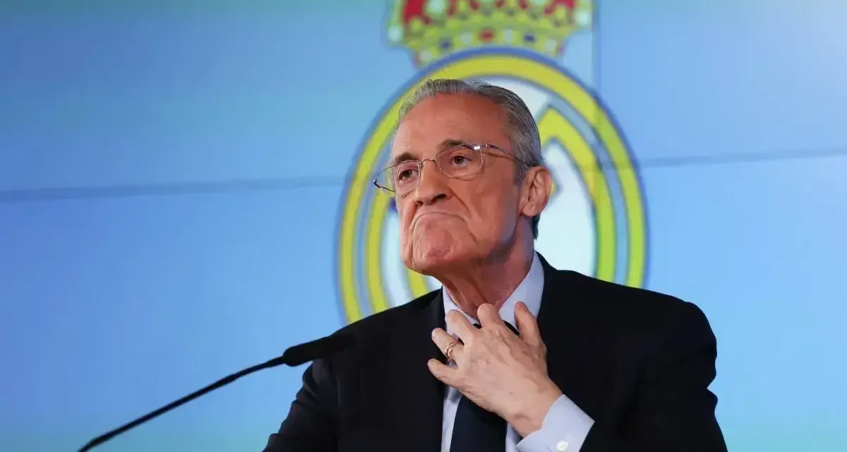 Florentino Pérez, prezes Realu Madryt, w garniturze, z ręką na szyi, na tle logo klubu.