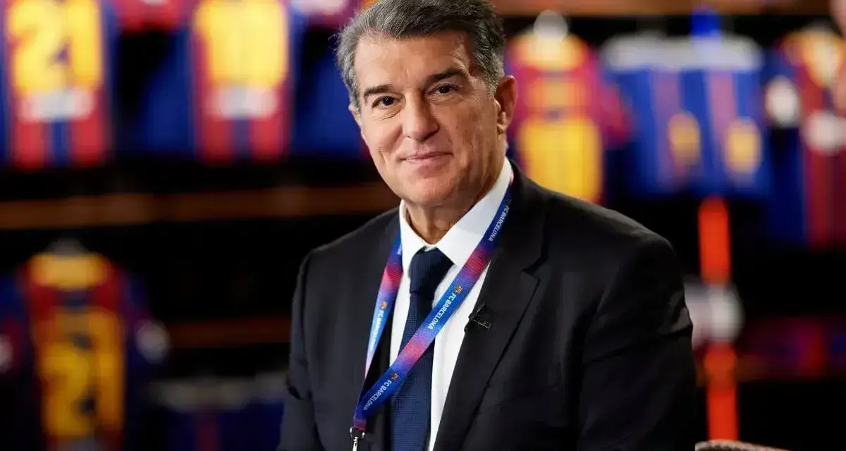 Uśmiechnięty prezes Barcelony, Joan Laporta, w garniturze, z identyfikatorem FC Barcelona na szyi.