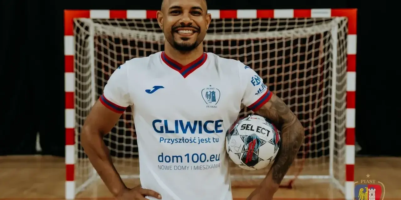 Piłkarz Piasta Gliwice w białej koszulce z piłką w ręku, na tle bramki.