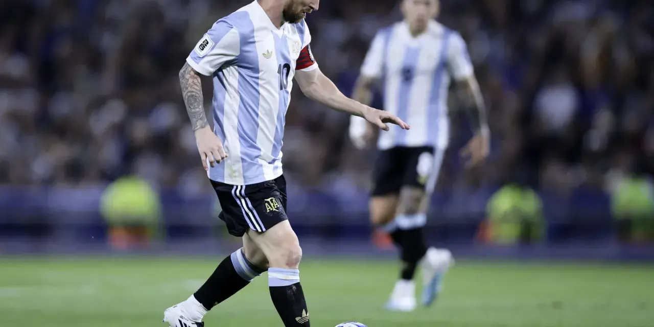Lionel Messi w koszulce Argentyny prowadzi piłkę, gotowy do zdobycia kolejnych bramek. Fani zastanawiają się, ile goli ma Messi.