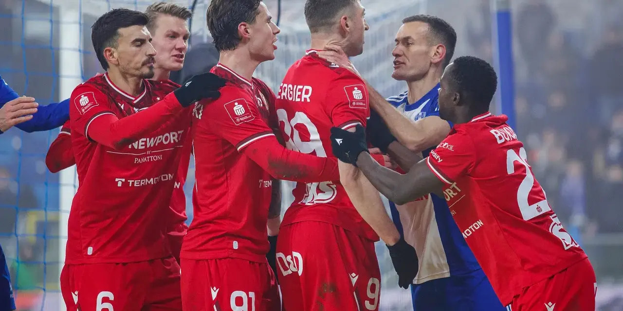 Piłkarze w czerwonych strojach kłócą się z zawodnikiem w niebieskiej koszulce.