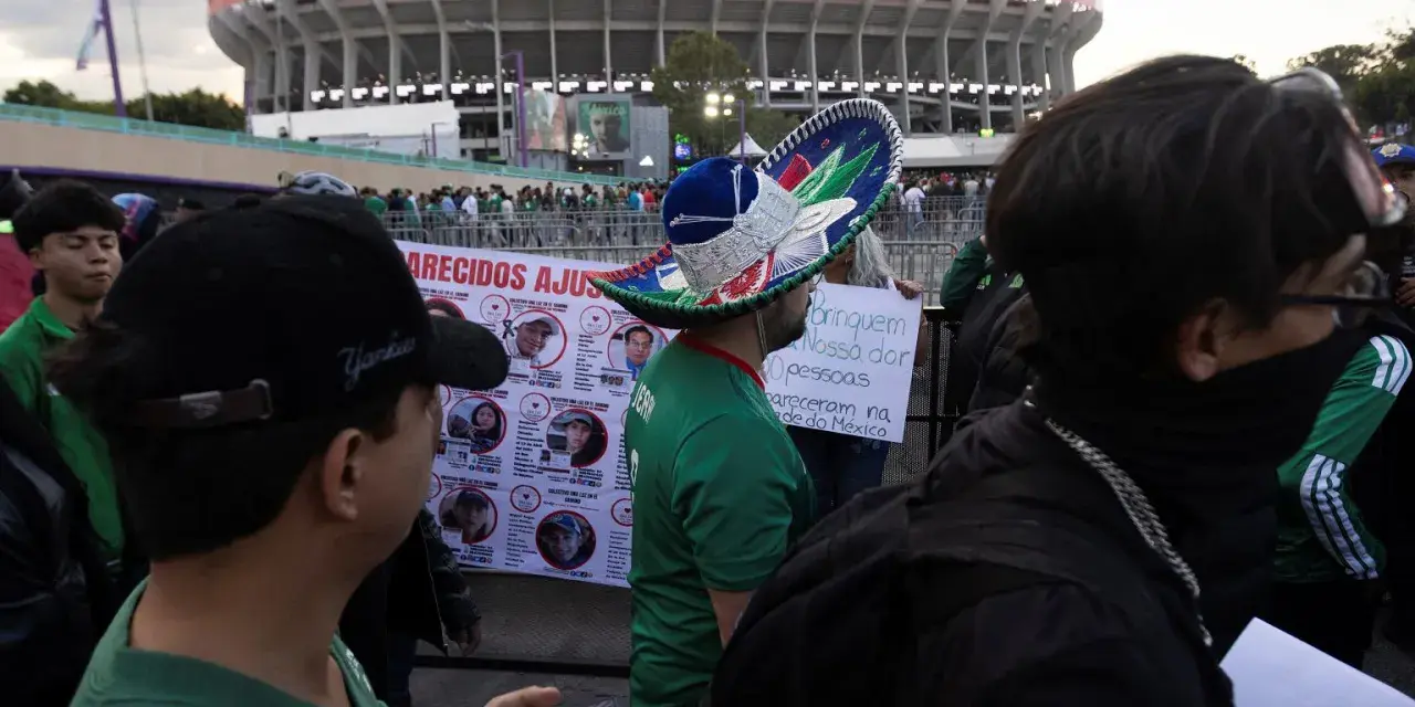 Tłum ludzi przed stadionem Azteca. Na pierwszym planie mężczyzna w meksykańskim kapeluszu, obok baner z portretami zaginionych.