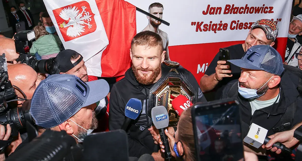 Jan Błachowicz, "Książę Cieszyński", mistrz UFC, otoczony przez fanów i dziennikarzy z polską flagą. Polacy w UFC świętują sukces.
