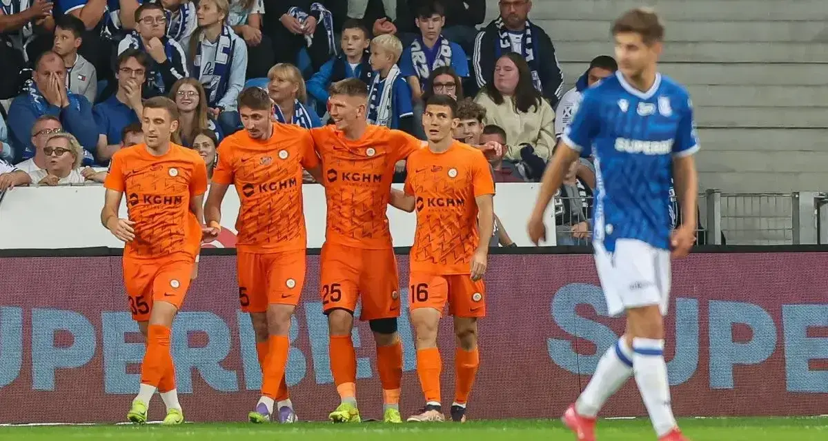 Piłkarze Zagłębia Lubin w pomarańczowych strojach świętują bramkę, podczas gdy zawodnik Lecha Poznań w niebieskim oddala się.