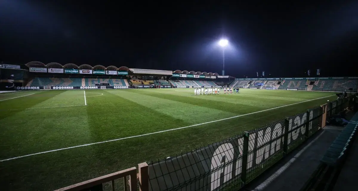 Piłkarze na murawie stadionu Górnik Łęczna, oświetlonego jupiterami.