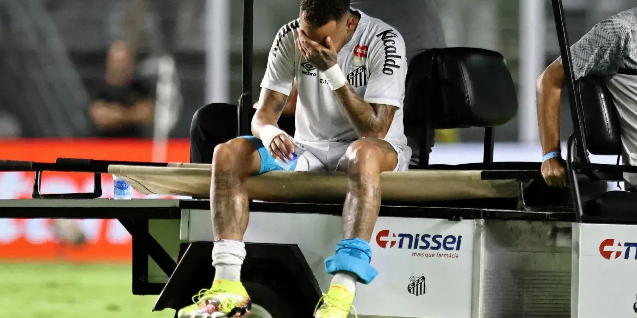 Neymar siedzi na wózku golfowym, zakrywając twarz dłońmi. Jego kontuzja jest widoczna, a zawodnik wygląda na zrozpaczonego.