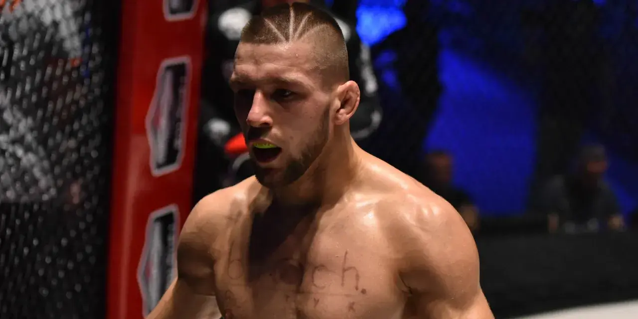 Zacięty zawodnik MMA z charakterystyczną fryzurą i ochraniaczem na zęby, gotowy do walki.