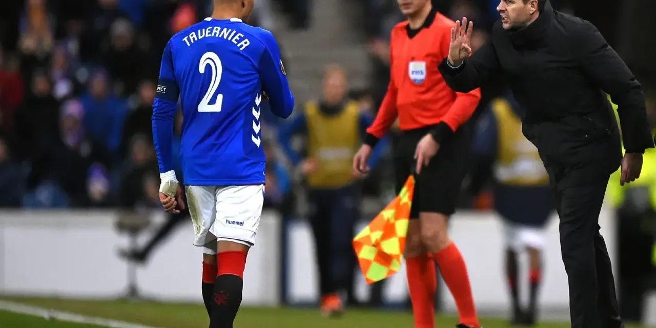 Piłkarz Rangers, Tavernier, słucha trenera. Sędzia liniowy z chorągiewką stoi obok.