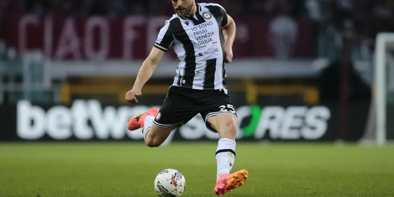 Piłkarz Jesper Karlström w czarno-białej koszulce Udinese Calcio kopie piłkę na zielonej murawie stadionu.