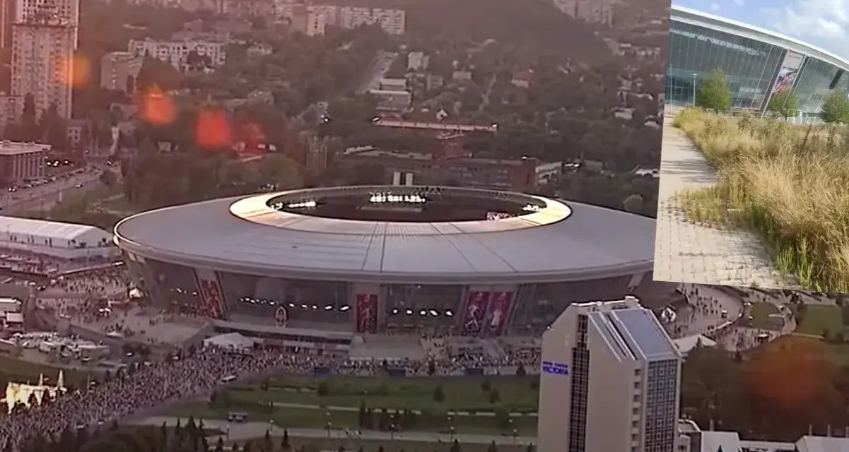 Donbass Arena w blasku zachodzącego słońca, otoczona miejskim krajobrazem i tłumami ludzi.