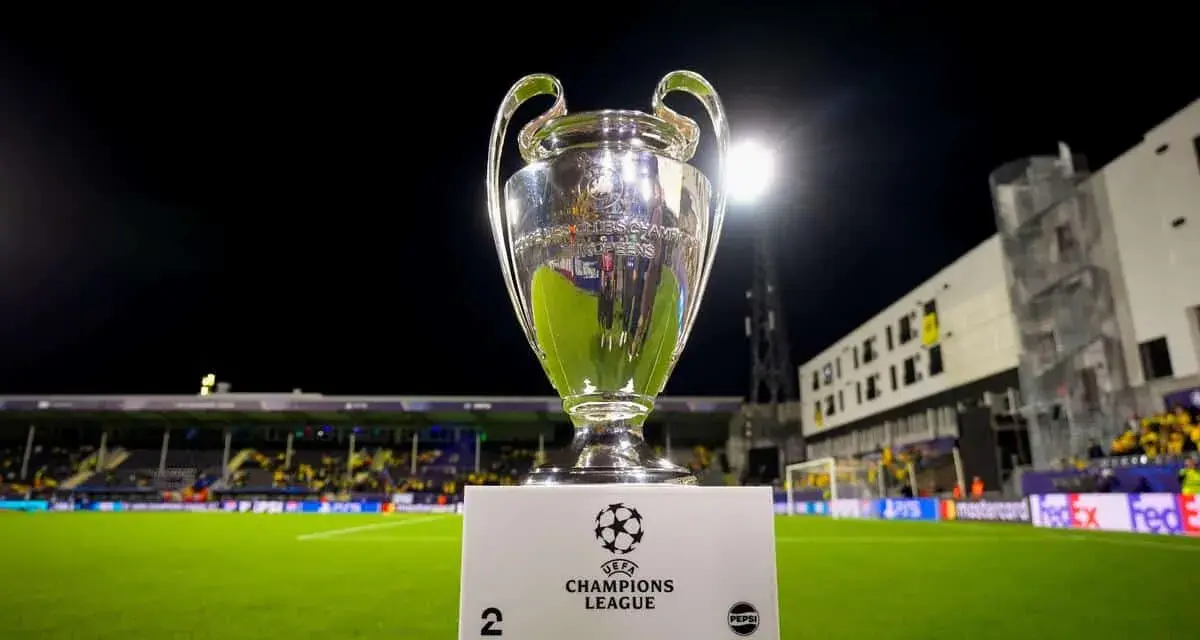 Puchar Ligi Mistrzów na tle stadionu. Ile drużyn awansuje do ligi mistrzów? To pytanie zadają sobie kibice.