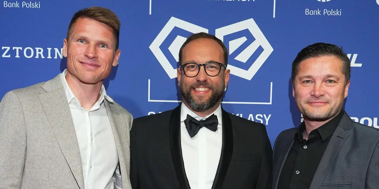 Trzech mężczyzn na tle PKO Bank Polski Ekstraklasa. Jeden z nich, w garniturze, uśmiecha się do obiektywu, być może jako jeden z przyszłych królowie strzelców ekstraklasy.
