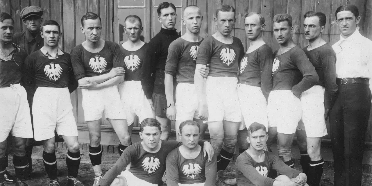 Drużyna piłkarska pozuje do zdjęcia. Widać, ile osób gra w piłkę nożną: 15 zawodników w strojach z orłem.