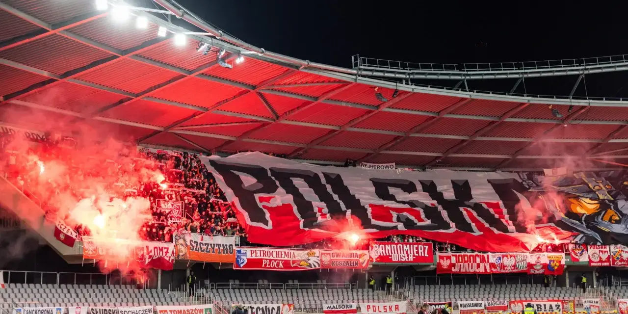 Tłum kibiców, ultrasi, tworzy morze czerwonego dymu i ognia, rozwijając ogromny transparent "POLSKA".