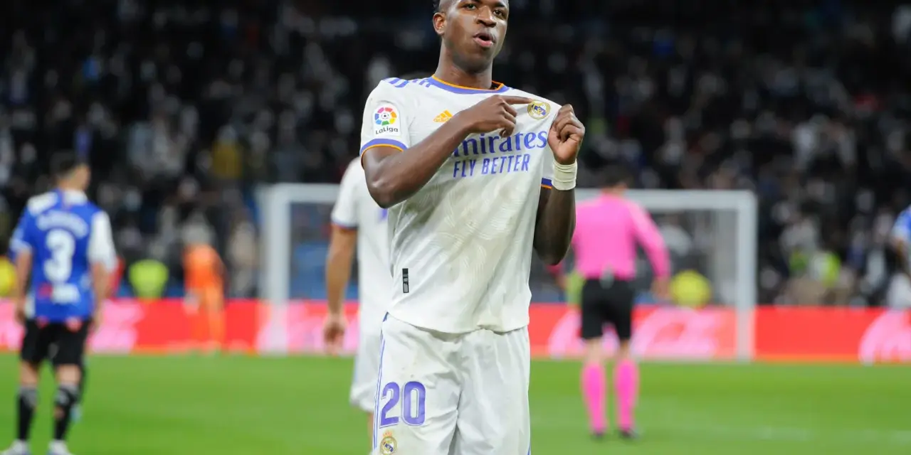 Vinicius Jr. w białej koszulce Realu Madryt z numerem 20, świętuje bramkę na tle trybun.