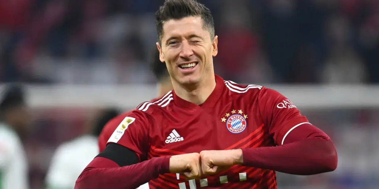 Piłkarz Robert Lewandowski w czerwonej koszulce Bayernu Monachium, uśmiecha się i zaciska pięści.