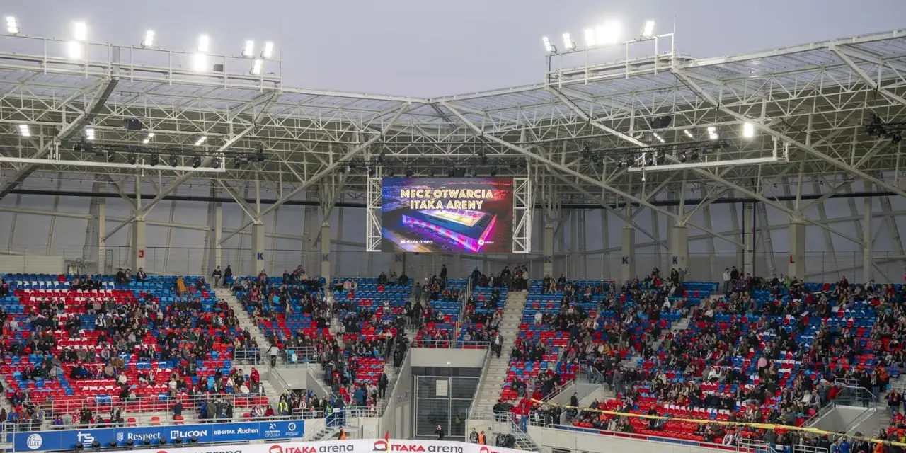 Widownia na stadionie Odra Opole podczas meczu otwarcia. Kolorowe trybuny i wielki ekran z napisem "Mecz otwarcia Itaka Areny".