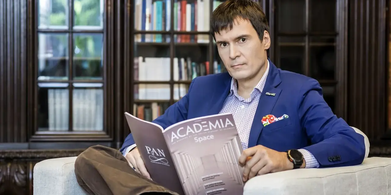 Mężczyzna w garniturze czyta magazyn "Academia Space" w bibliotece. W tle regały z książkami.