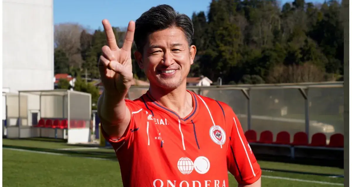 Uśmiechnięty Kazuyoshi Miura, najstarszy piłkarz na świecie, pokazuje znak pokoju na boisku.