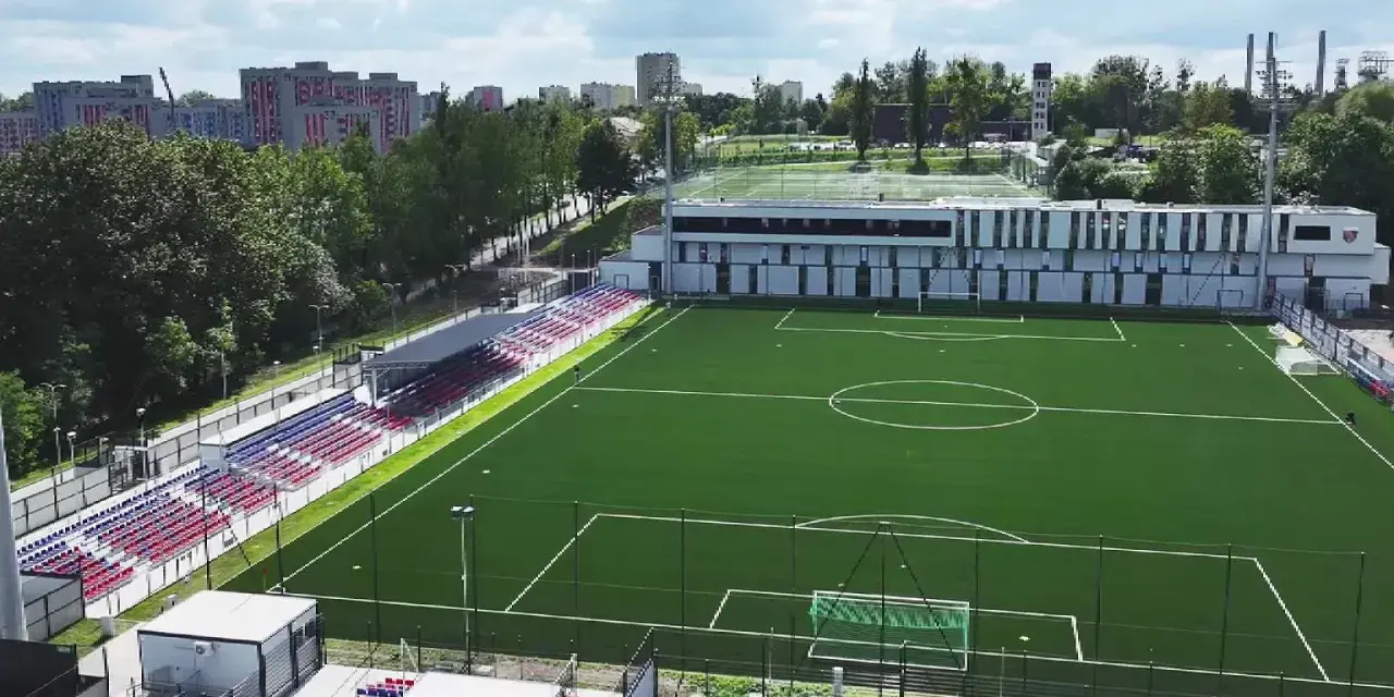 Nowy stadion Polonii Bytom z zieloną murawą, trybunami w kolorach czerwonym i niebieskim oraz nowoczesnym budynkiem klubowym.
