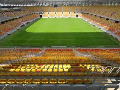 Pusta trybuna stadionu Jagiellonii, z żółtymi i czerwonymi siedzeniami. Pojemność obiektu robi wrażenie.