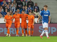 Piłkarze Zagłębia Lubin w pomarańczowych strojach świętują bramkę, podczas gdy zawodnik Lecha Poznań w niebieskim oddala się.