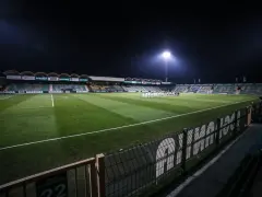 Piłkarze na murawie stadionu Górnik Łęczna, oświetlonego jupiterami.