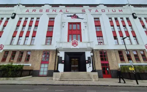 Dawny stadion Arsenalu w Highbury, z charakterystycznym napisem "ARSENAL STADIUM" i czerwonymi akcentami.